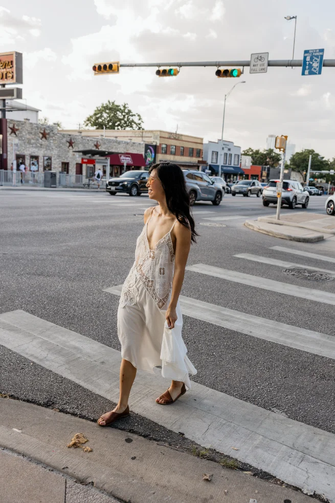 Florence Wong crossing a sunny Austin street in a white dress