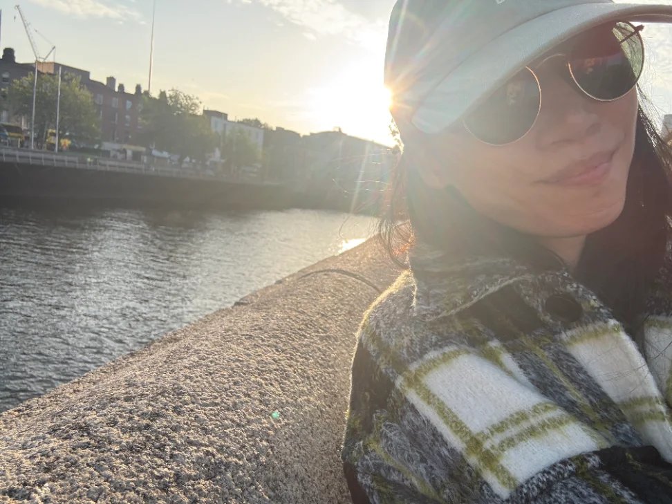 Florence, founder of The Prickly Pear Collected, in a cap and sunglasses beside a river at sunset
